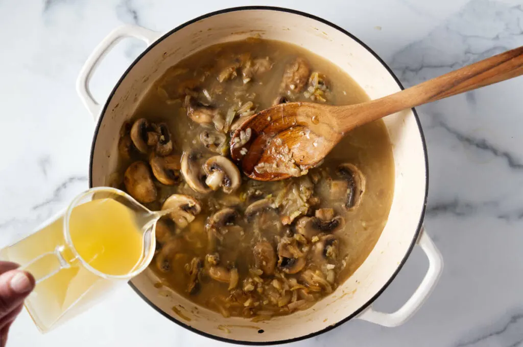 Pouring chicken broth into the skillet with mushrooms.