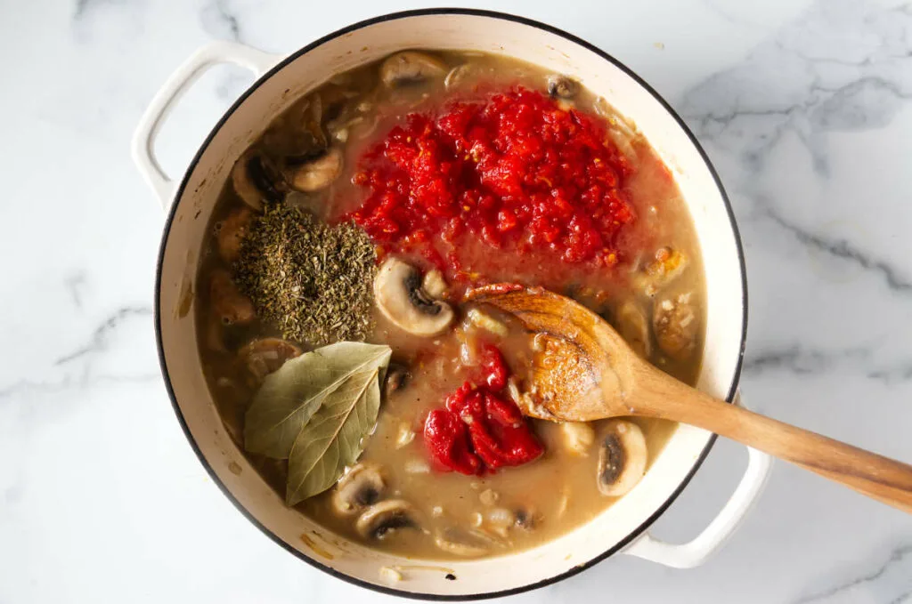 Stirring herbs and tomatoes into the sauce.