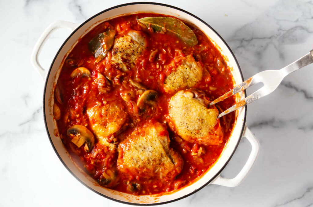 Adding the chicken thighs to the tomato sauce.