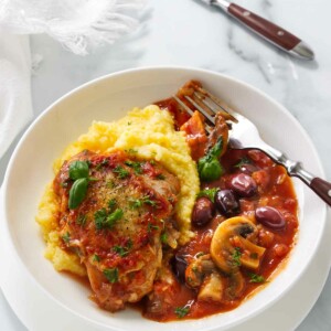 A serving of authentic chicken cacciatore with mushrooms over a bed of polenta.