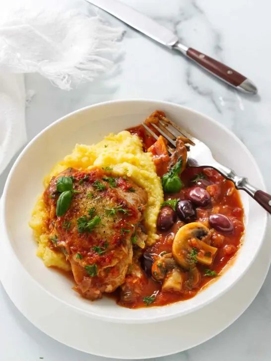 A serving of authentic chicken cacciatore with mushrooms over a bed of polenta.