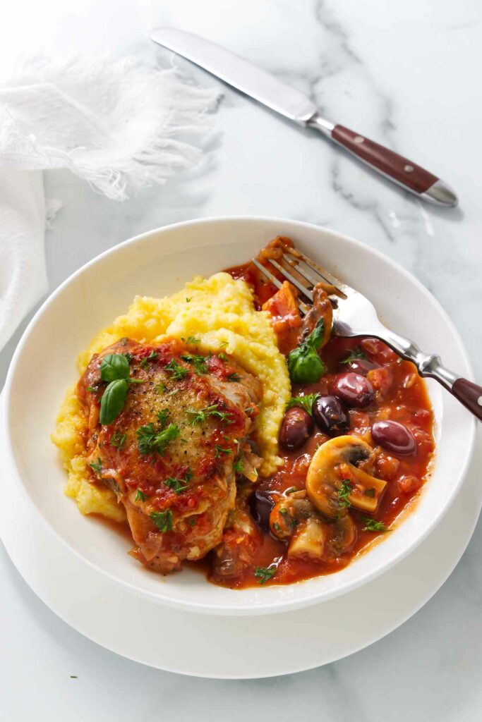 A serving of authentic chicken cacciatore with mushrooms over a bed of polenta.