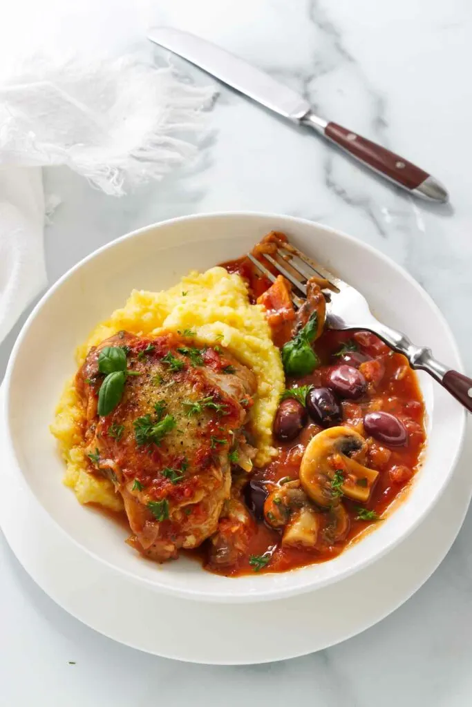 A serving of authentic chicken cacciatore with mushrooms over a bed of polenta.