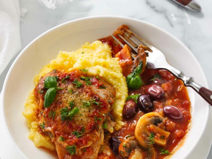 A serving of authentic chicken cacciatore with mushrooms over a bed of polenta.