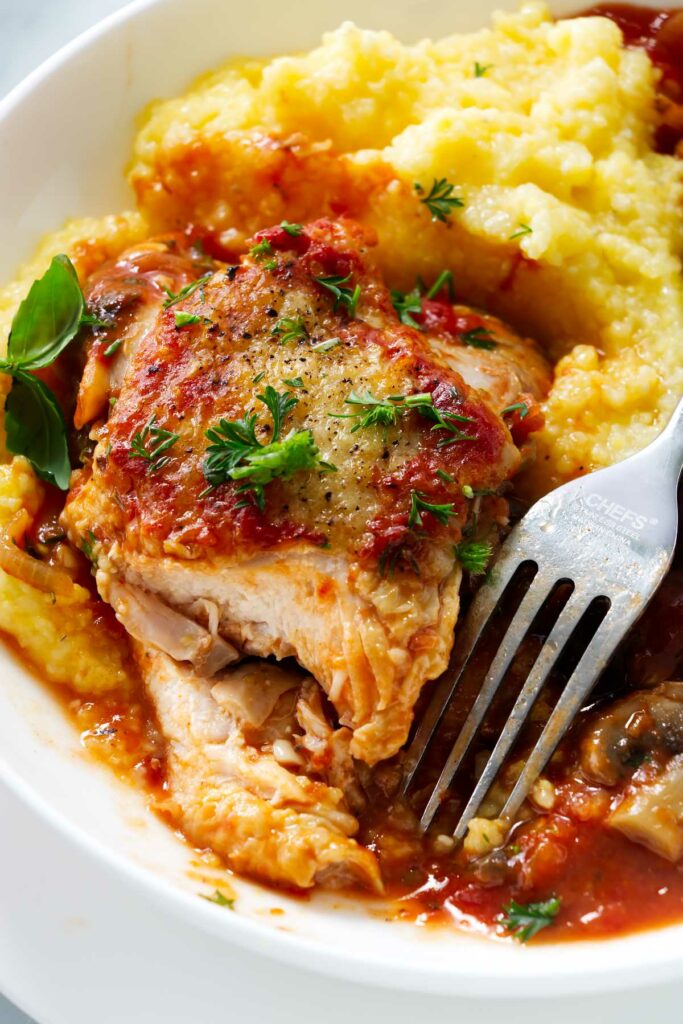 Chicken breast with cacciatore sauce on a bed of polenta next to a fork.