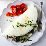 An egg white omelette on a plate with a fork and diced tomatoes.