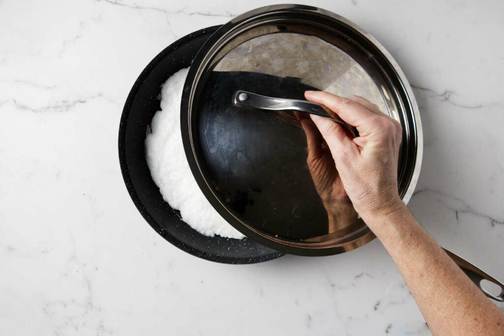 Placing a lid over the egg whites in a skillet.