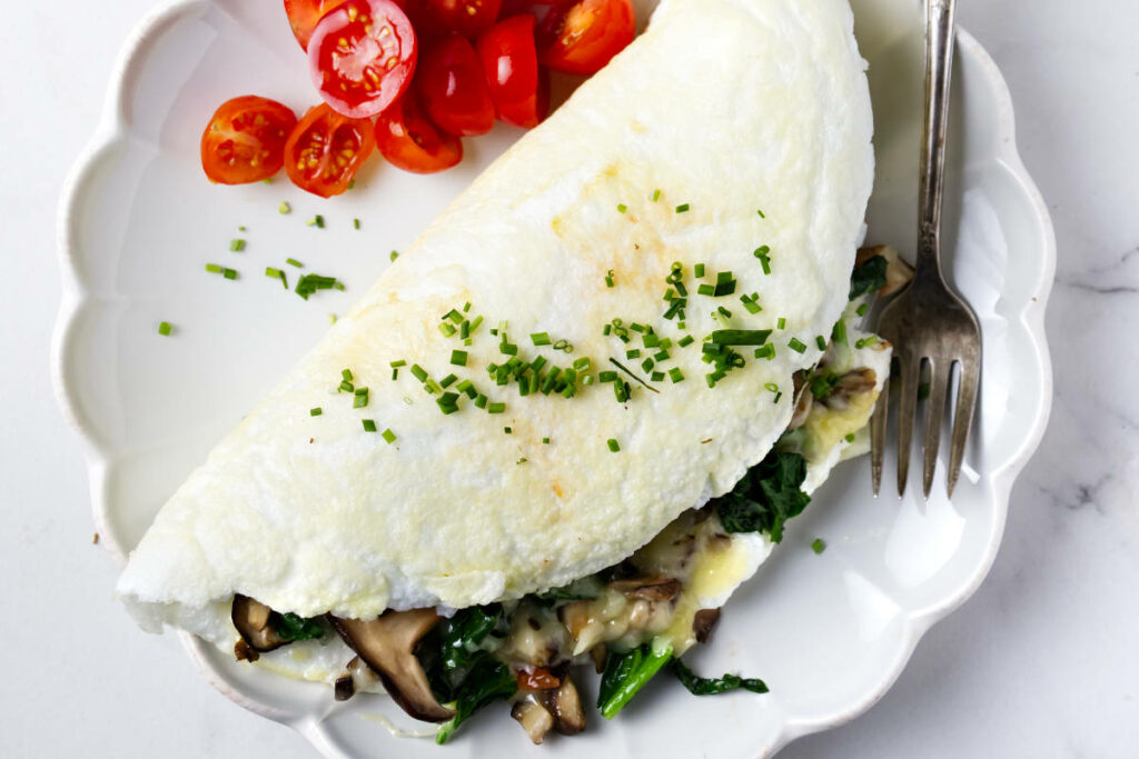 A fluffy souffle style egg white omelet on a plate with diced tomatoes.