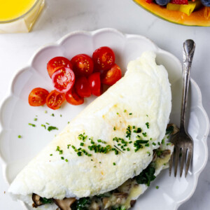 An egg white omelet on a plate with sliced tomatoes next to a papaya filled with berries.