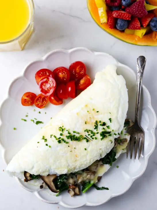 An egg white omelet on a plate with sliced tomatoes next to a papaya filled with berries.