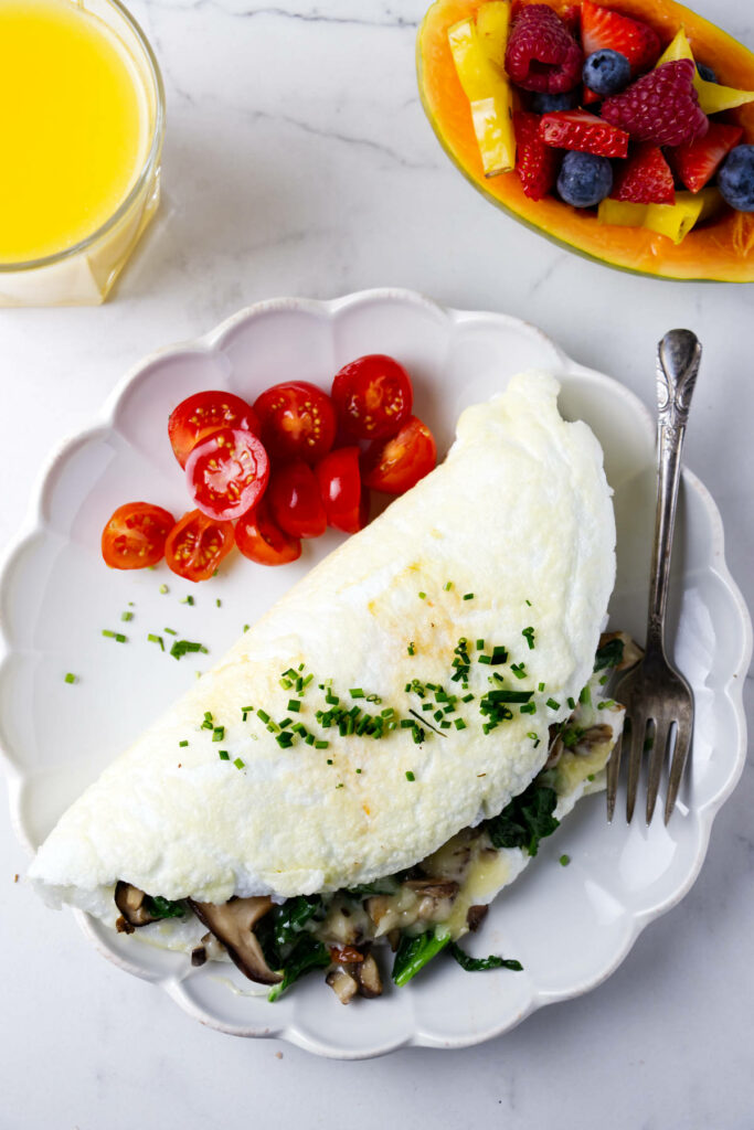 An egg white omelet on a plate with sliced tomatoes next to a papaya filled with berries.