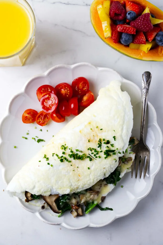 An egg white omelet on a plate with sliced tomatoes next to a papaya filled with berries.