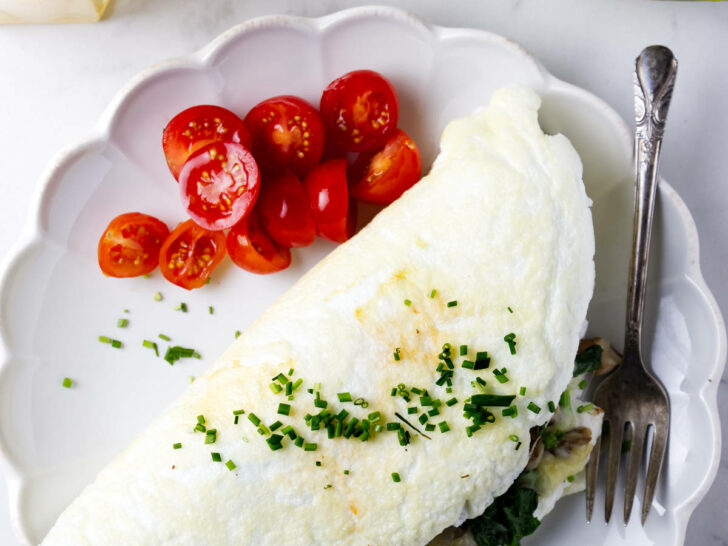 An egg white omelet on a plate with sliced tomatoes next to a papaya filled with berries.