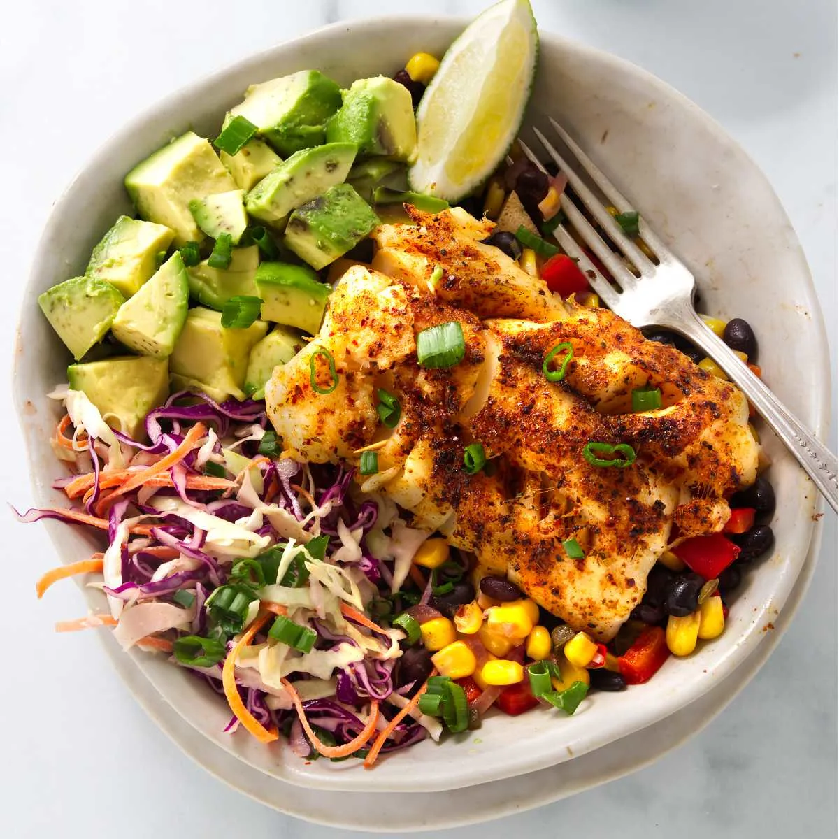 A bowl filled with a pan fried cod over corn and bean salsa with slaw and avocado.