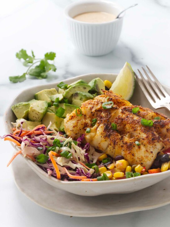 A fish taco bowl with cod and black bean salsa in front of a dish of taco sauce.