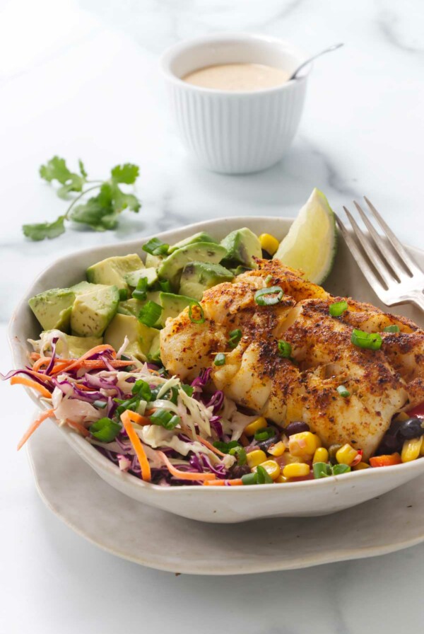 A fish taco bowl with cod and black bean salsa in front of a dish of taco sauce.