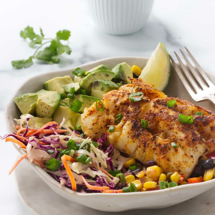 A fish taco bowl with cod and black bean salsa in front of a dish of taco sauce.