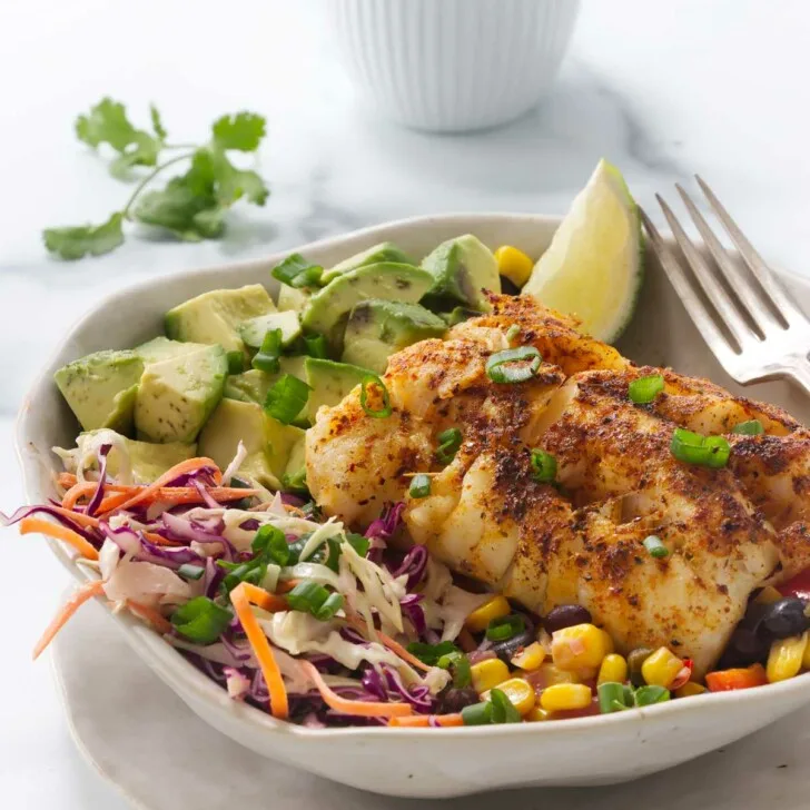 A fish taco bowl with cod and black bean salsa in front of a dish of taco sauce.