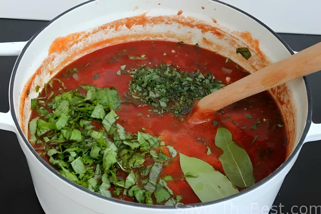 Adding fresh herbs to a pot to simmer with tomato sauce.