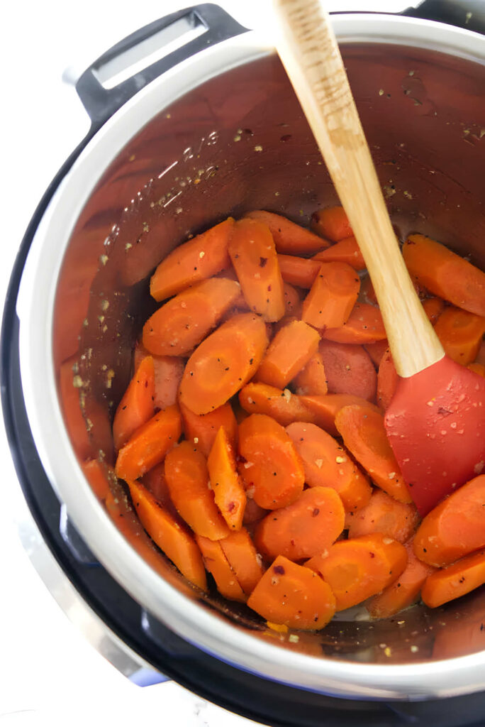 An instant pot with sliced carrots and a large spatula to stir the glaze.