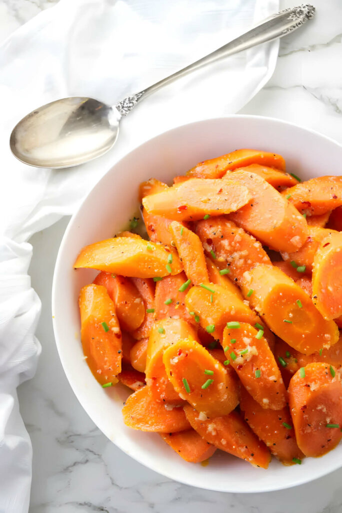 A serving spoon next to a bowl of honey glazed carrots.