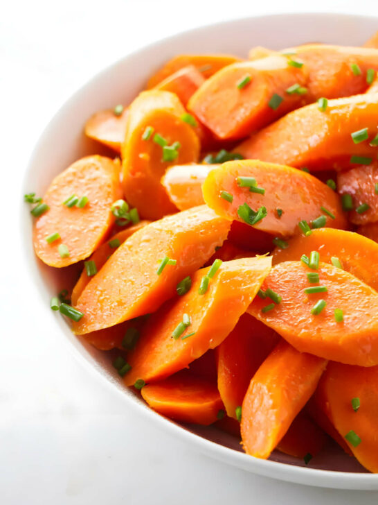 A serving bowl filled with steamed carrots garnished with chives.