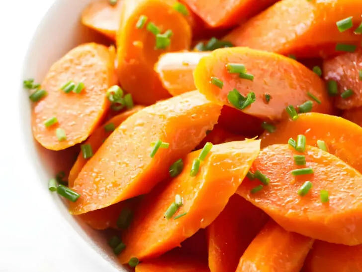 A serving bowl filled with steamed carrots garnished with chives.