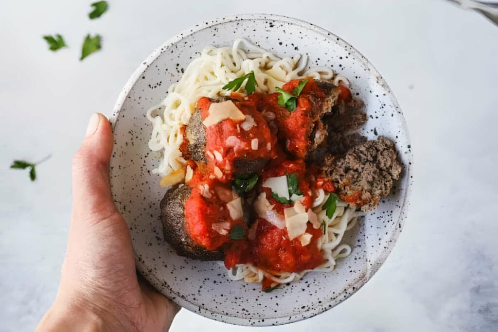 A hand holding a dish with meatballs and low carb noodles.