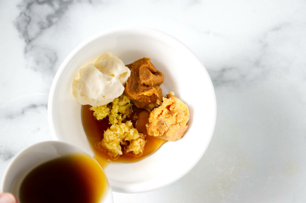 Pouring oil into a dish with miso-ginger dressing ingredients.