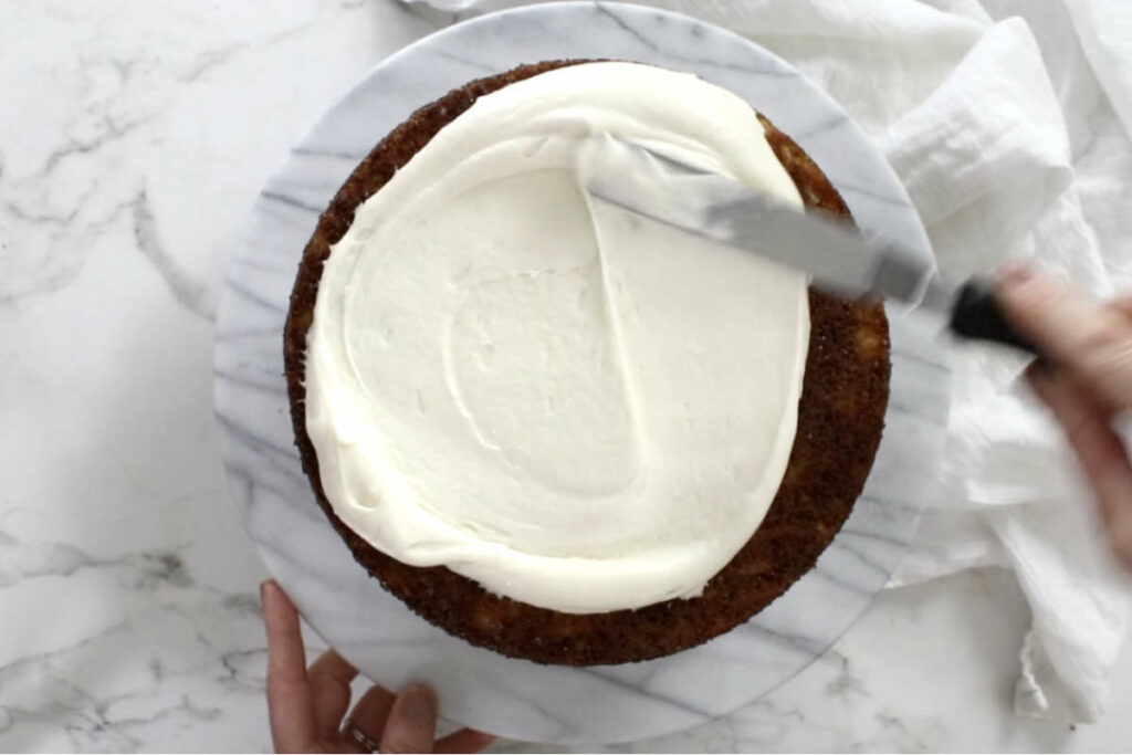 Spreading a cake with cream cheese frosting.