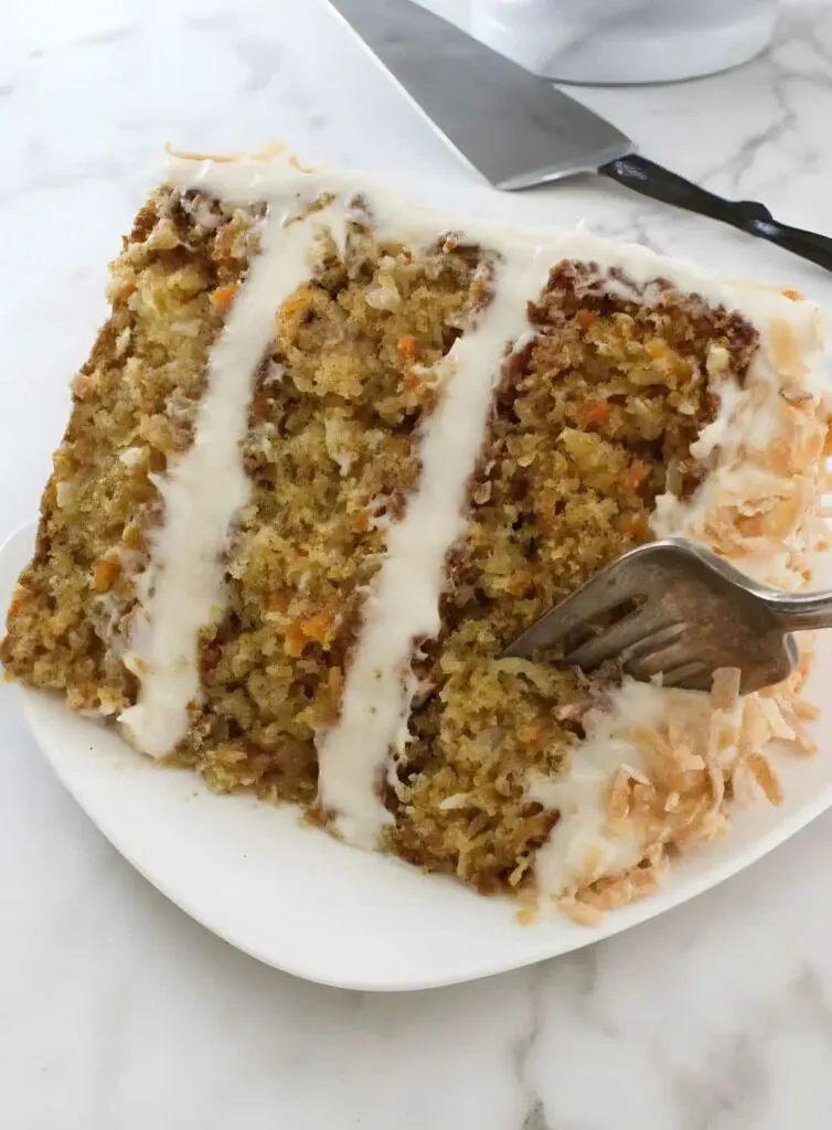 A fork taking off a section of a three layer carrot cake.