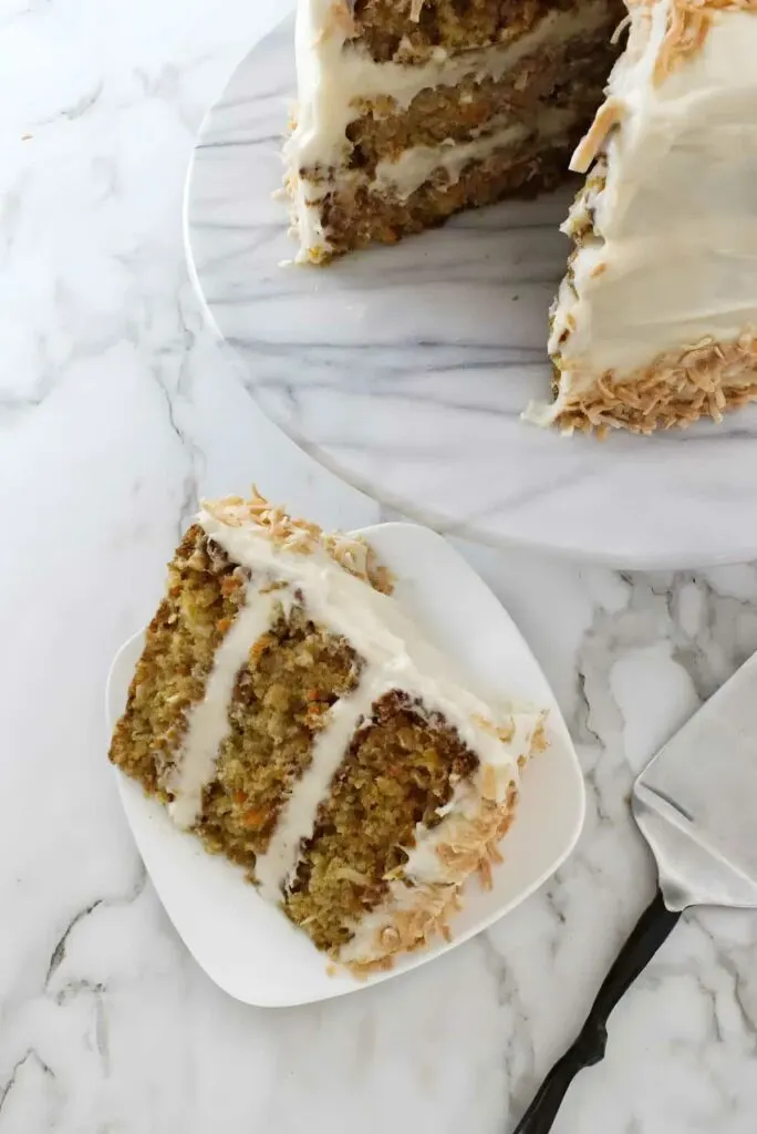 A slice of carrot cake next to a cake on a platter.