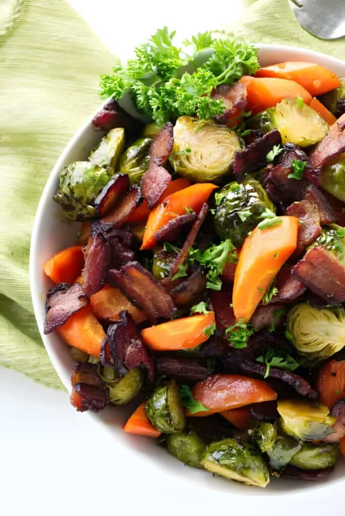 A white bowl filled with sliced brussels sprouts and carrots with bacon.