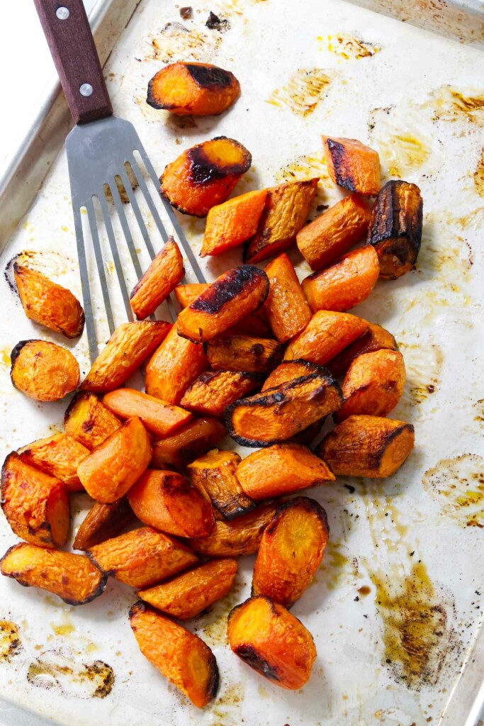 A spatula scooping up baked carrots from a sheet pan.