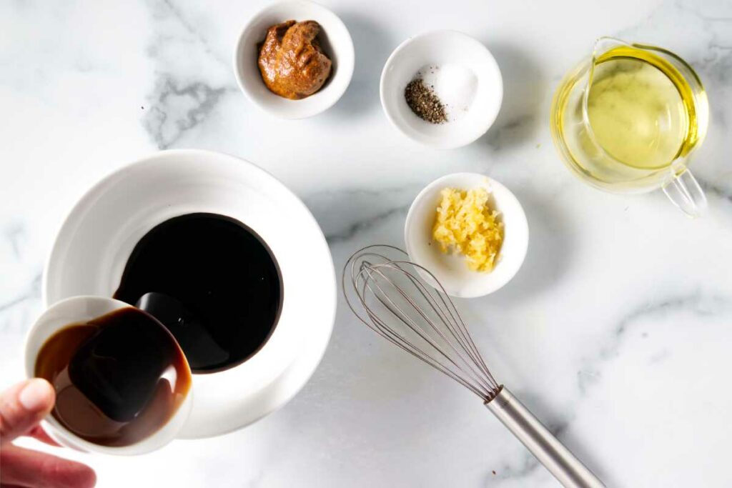 Combining balsamic vinegar in a mixing bowl next to a whisk.