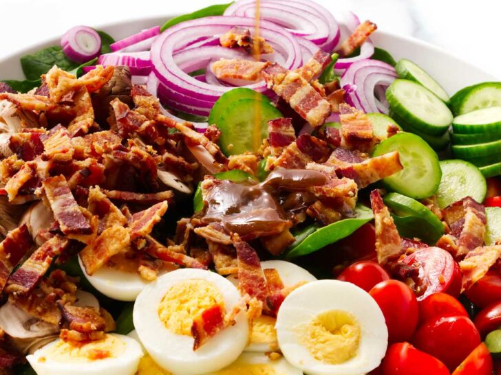 Pouring balsamic vinaigrette over a spinach bacon salad with tomatoes and eggs.