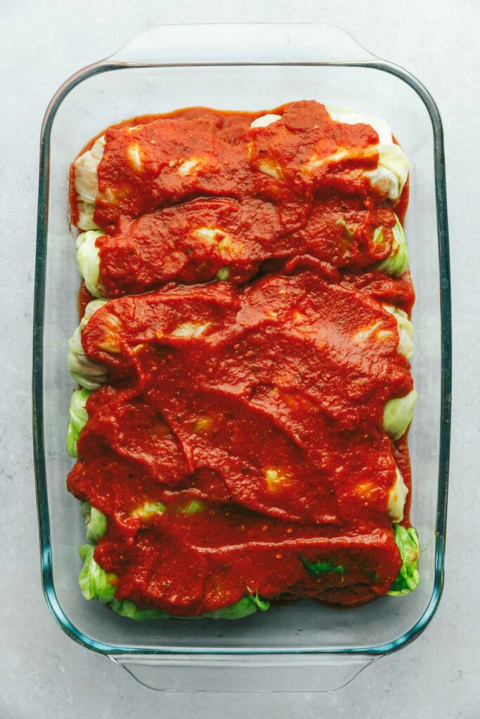 Stuffed cabbage leaves in a casserole dish covered in tomato sauce.