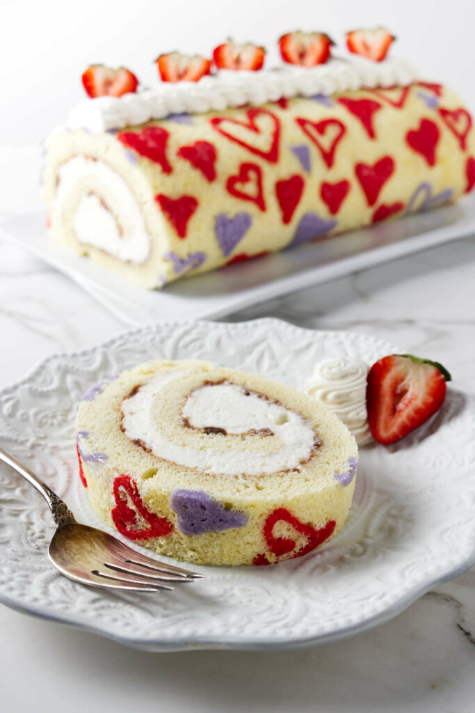 A heart roll cake on a plate with a slice in front with a fork.