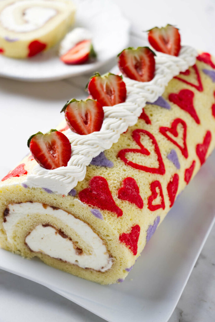 A valentine cake strawberry cake roll on a serving platter.