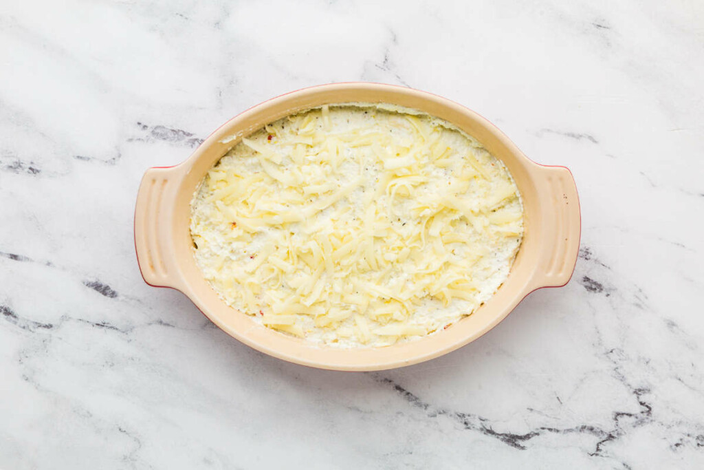 Adding shredded cheese to the top of a ricotta dip.