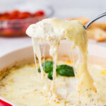 A spoon scooping a savory ricotta dip from a baking dip.