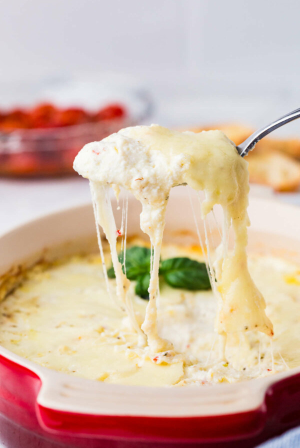 A spoon scooping a savory ricotta dip from a baking dip.