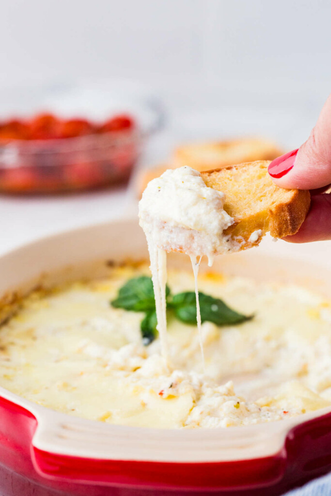 Ricotta cheese spread on bread with tomatoes in the background.