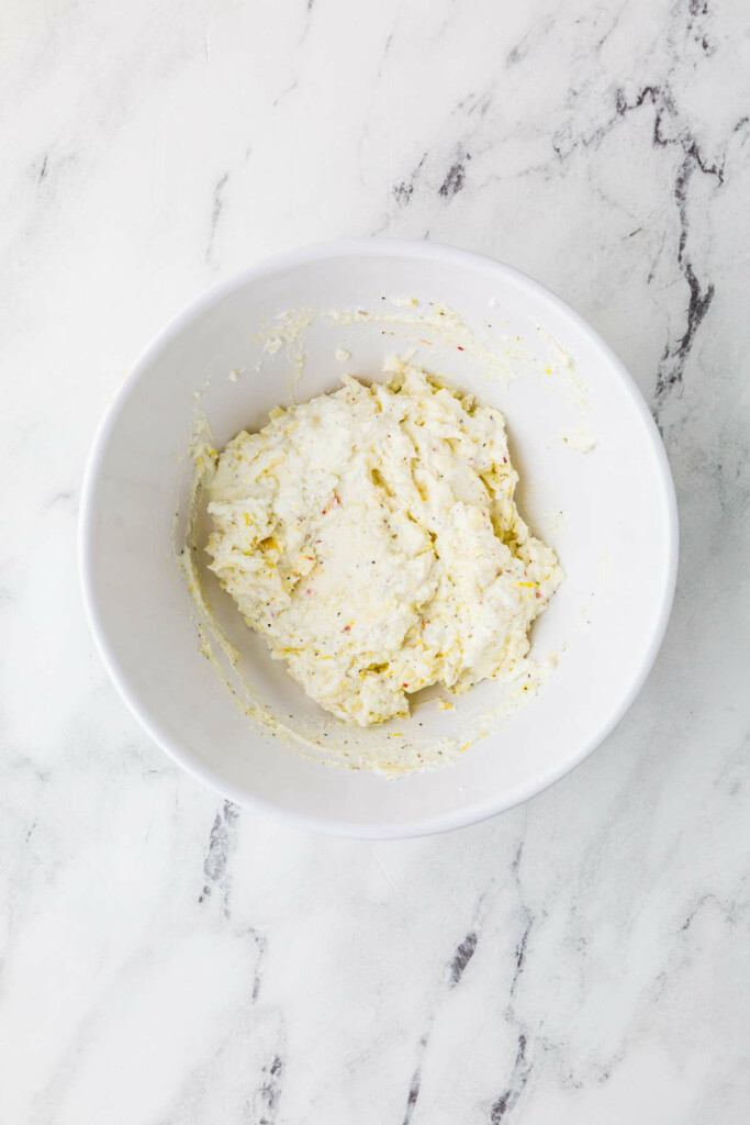 Mixing ricotta cheese with shredded cheese.