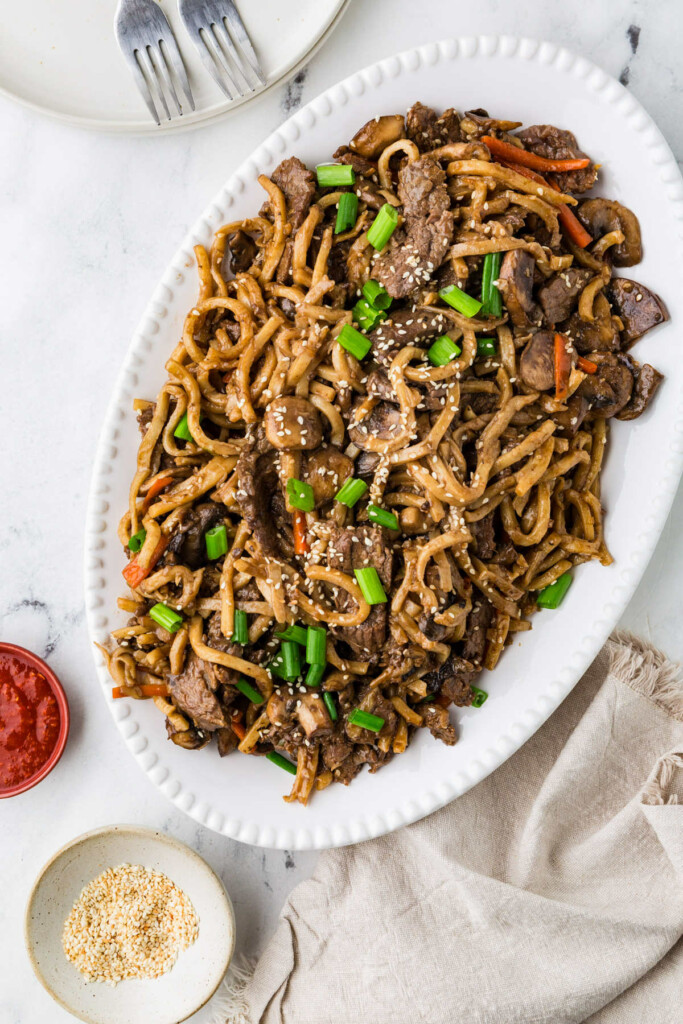 Beef udon noodles on a serving platter next to a dish of sesame seeds.