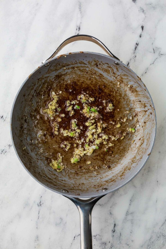 Adding garlic, ginger, and scallions to a hot skillet.