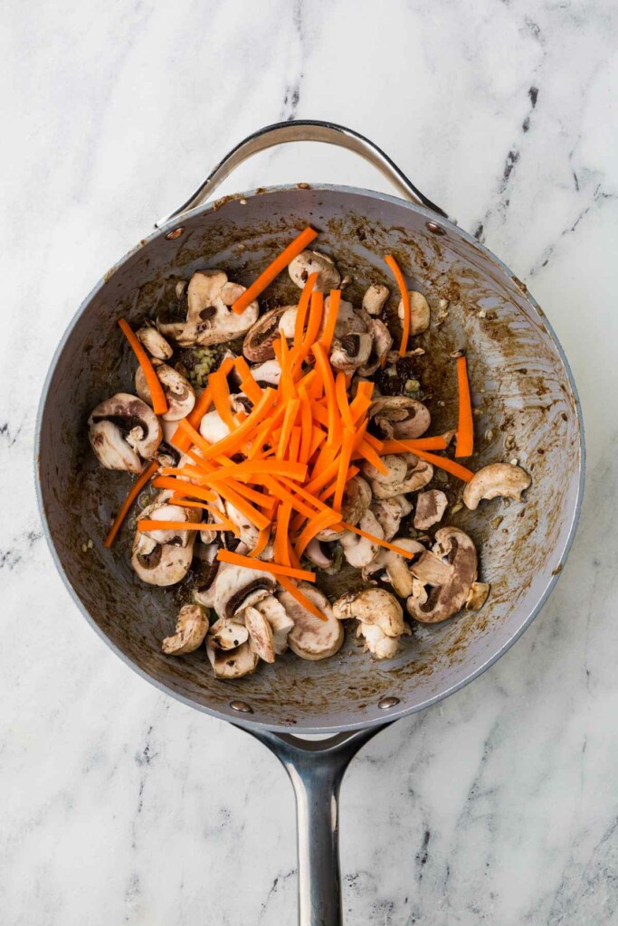 Adding carrots and mushrooms to the skillet for Japanese beef noodles.