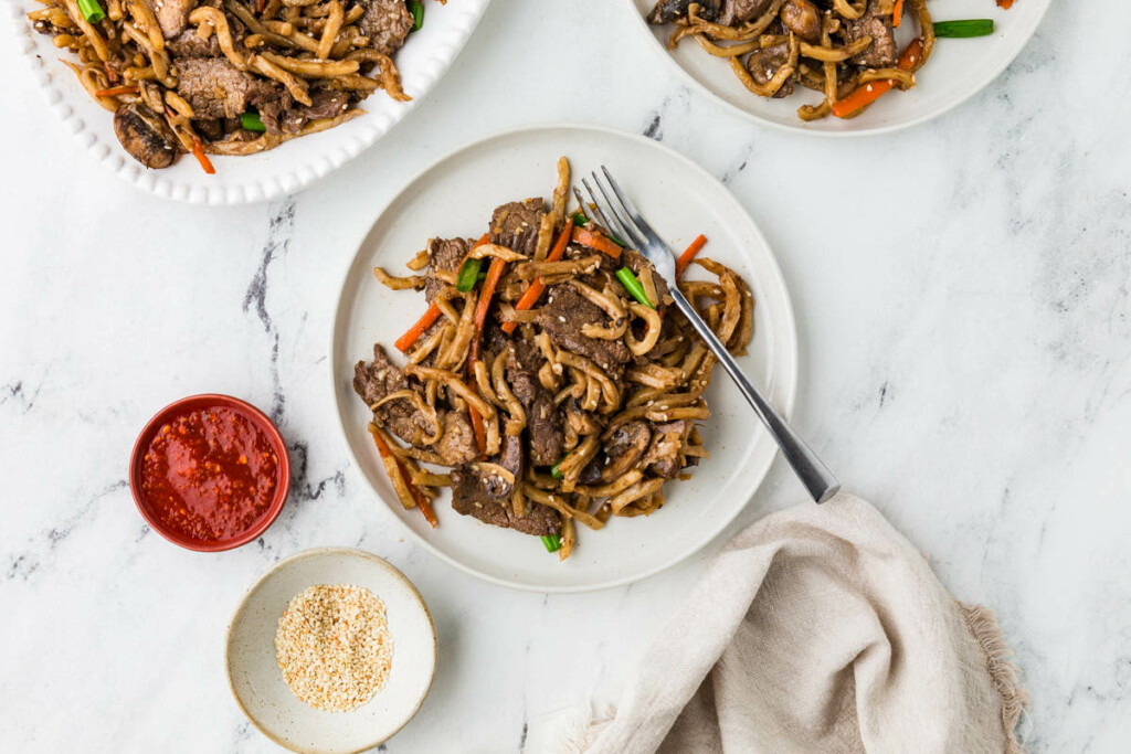 Beef udon stir fry on a plate with a fork.