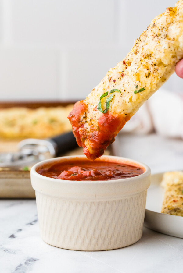 Cheesy breadsticks with pizza dough being dipped into red sauce.