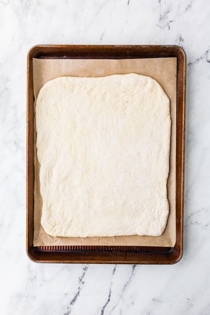 Stretching pizza dough into a rectangle on a sheet pan.